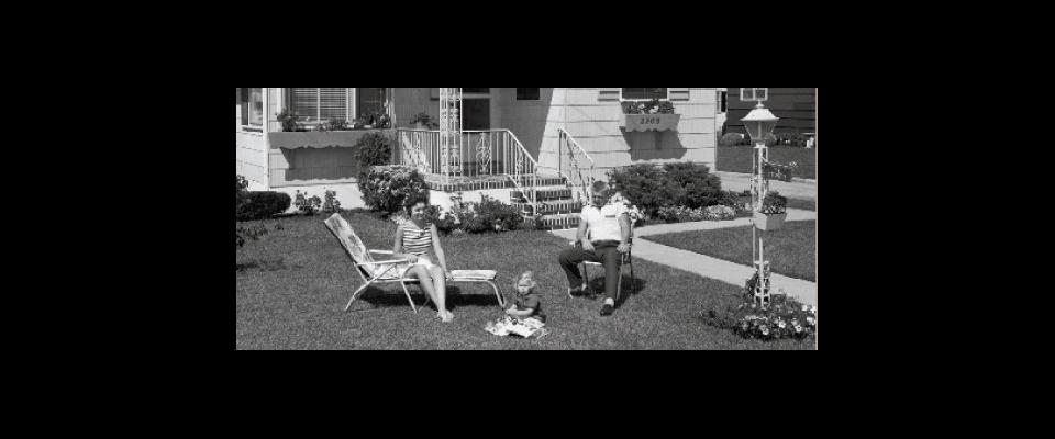 a black and white photograph of a couple on their front lawn with a child