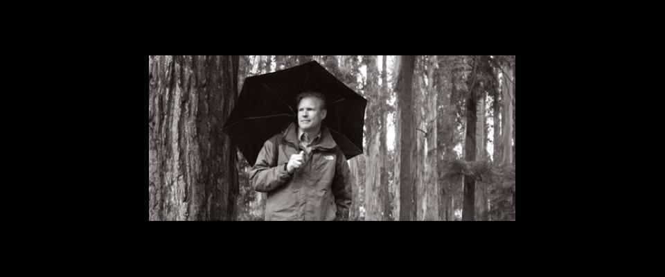 black and white photograph of Jim Horner under an umbrella in the forrest