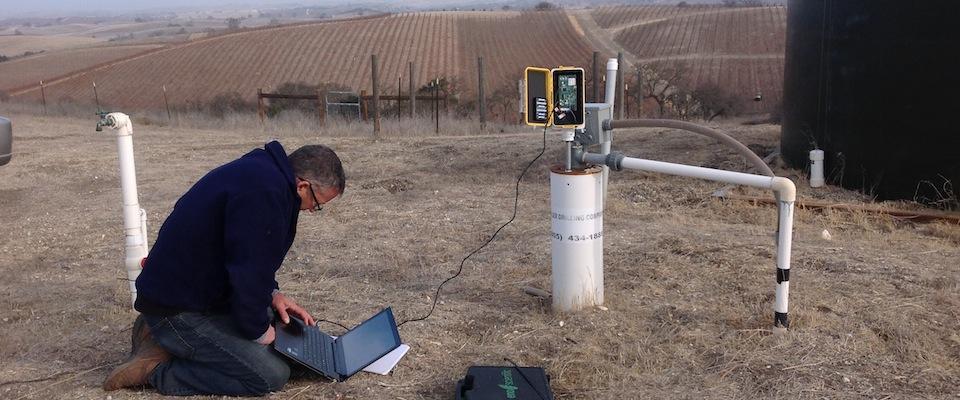 Farm worker kneeling near equipment that measure water underground