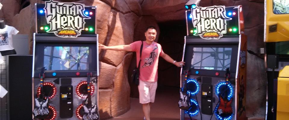Huang standing next to two guitar hero arcades