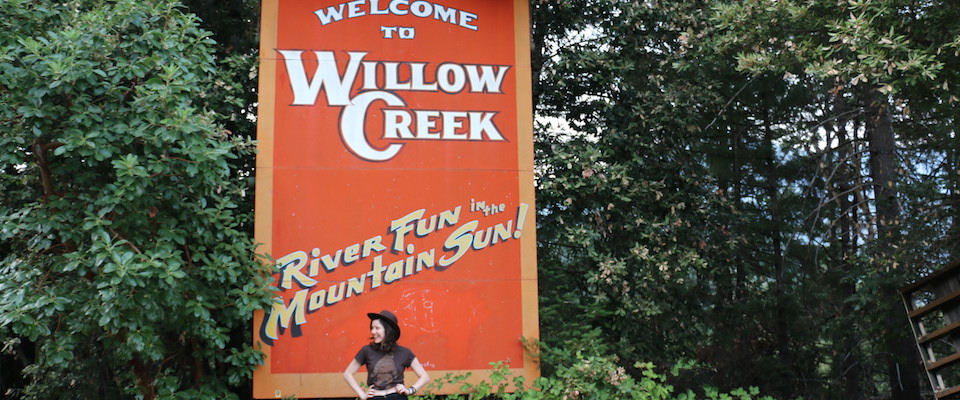 Person sitting in front of Welcome to Willow Creek sign
