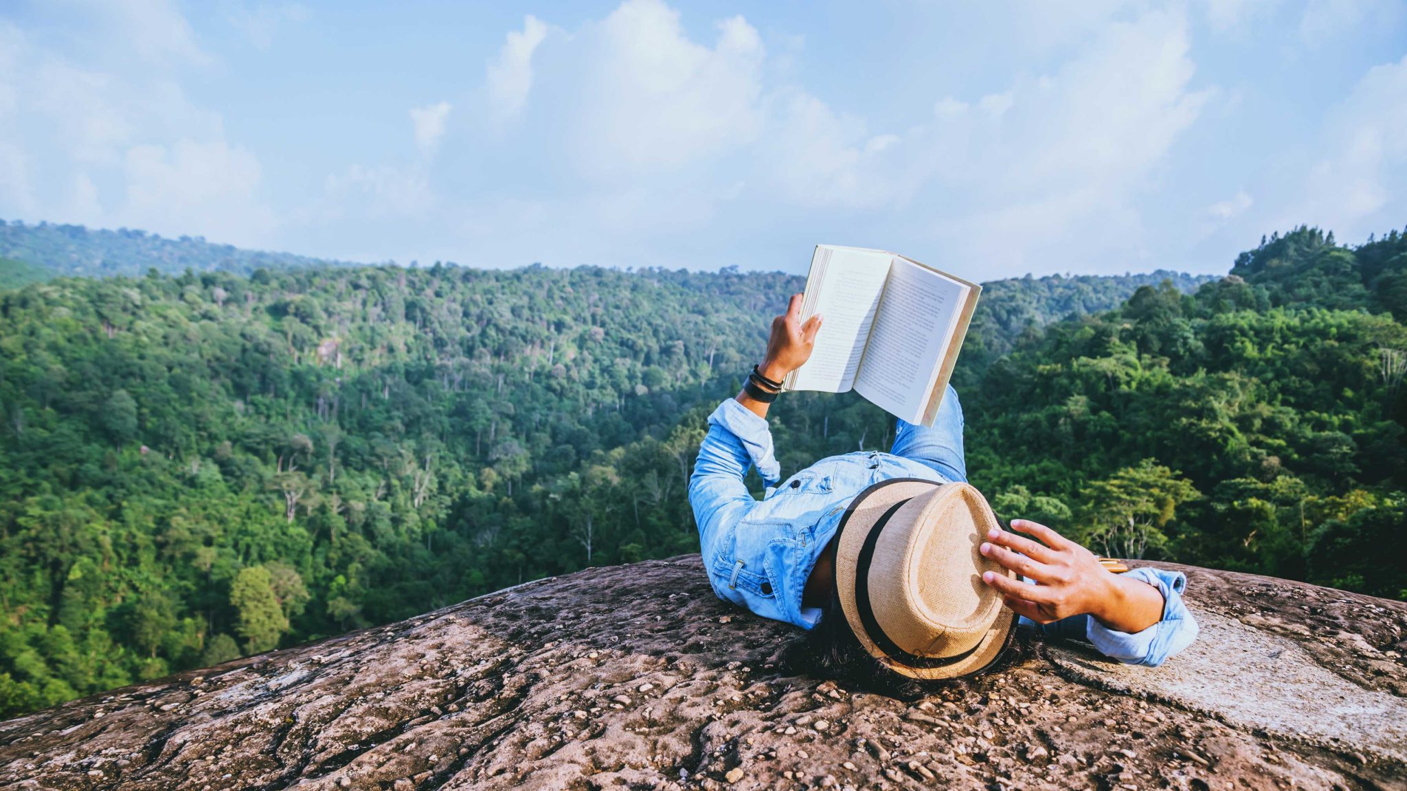 person laying down reading book above forest