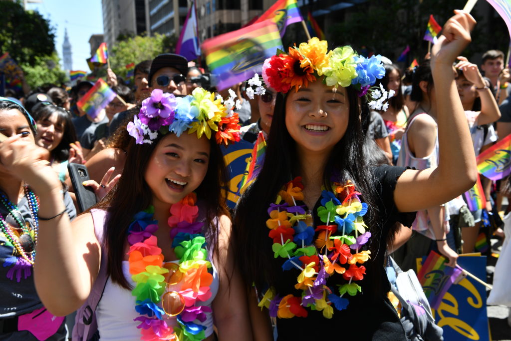 2 people waving rainbow pride flags in the middle of a parade