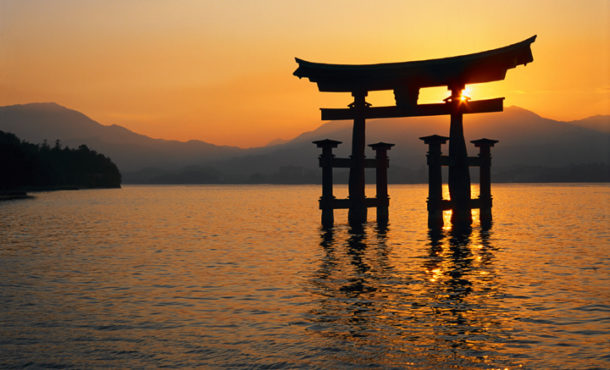 wooden structure standing in body of water in front of sunset