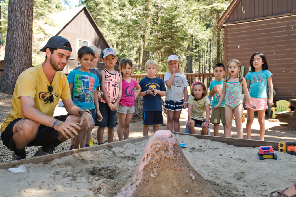 kids and staffer making a volcano in the sandbox