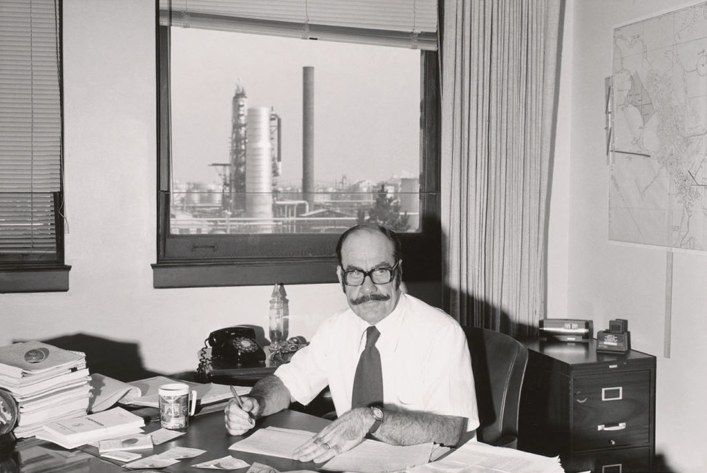 man sitting at his office near an oil refinery