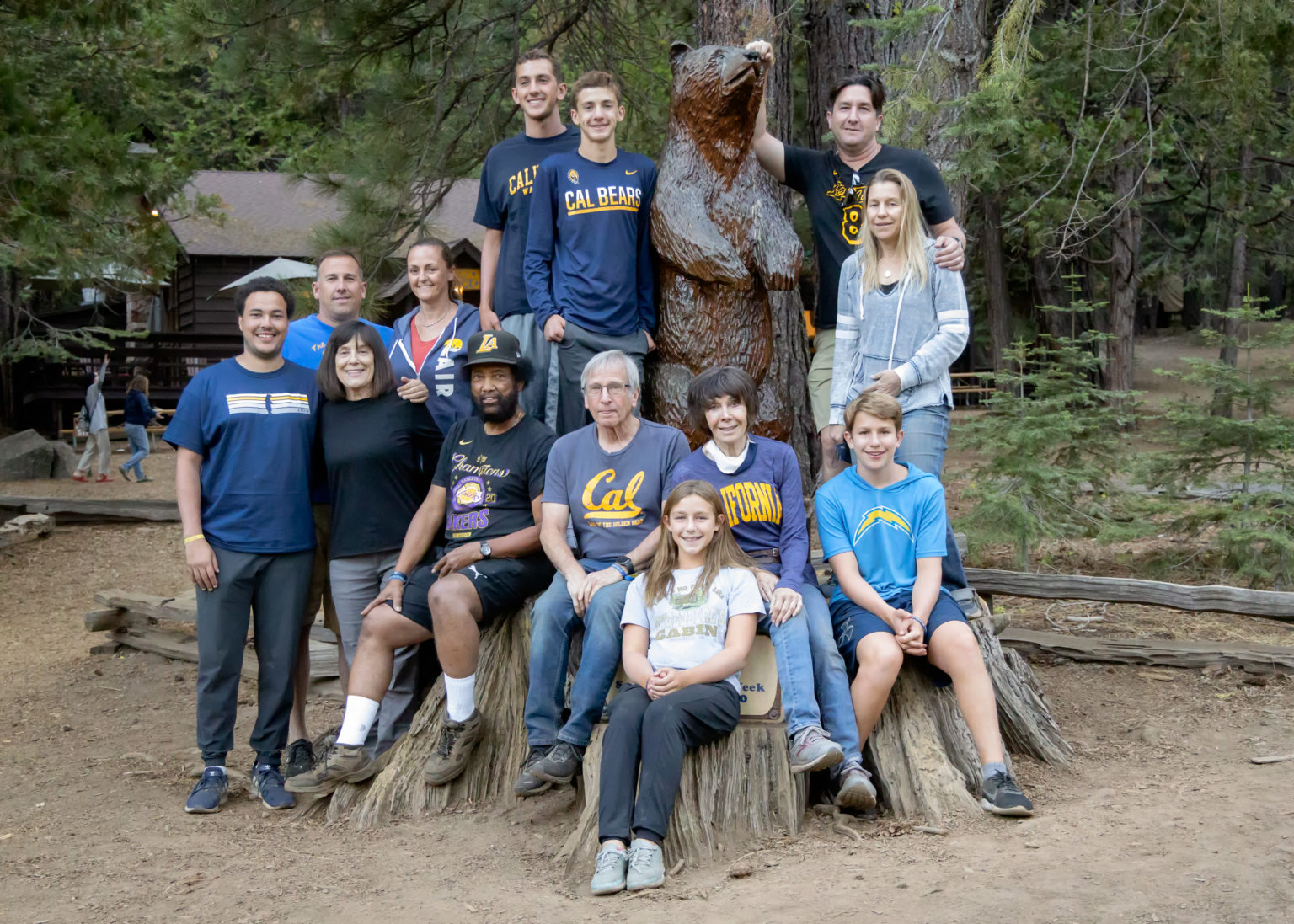 A multi-generational family dressed in Cal garb and blue and gold posing for a family portrait in front of the wooden Bear statue in camp.