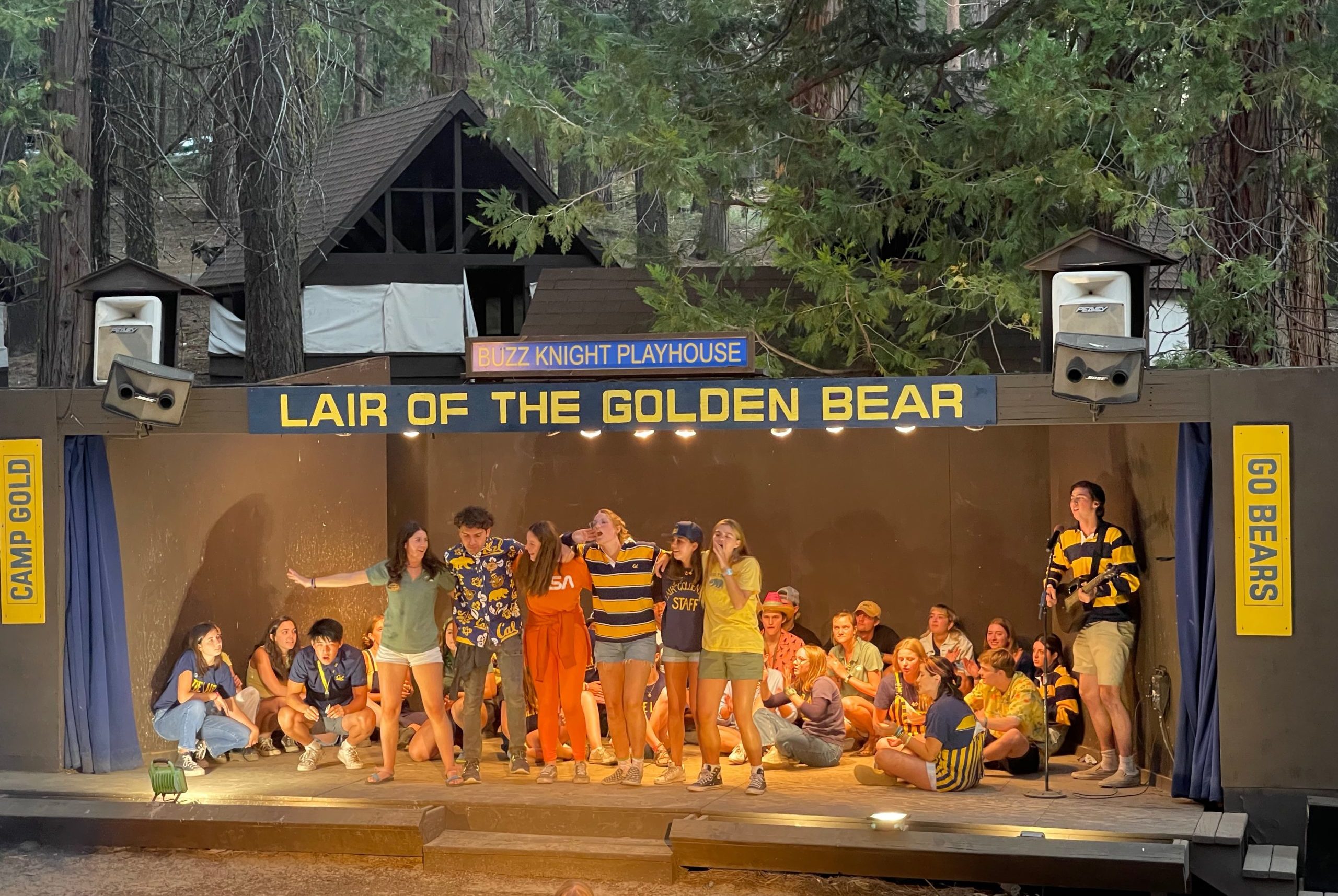 Lair staffers, dressed in blue and gold, singing on stage during the Saturday night show. One staffer is playing the guitar and 5 are singing.
