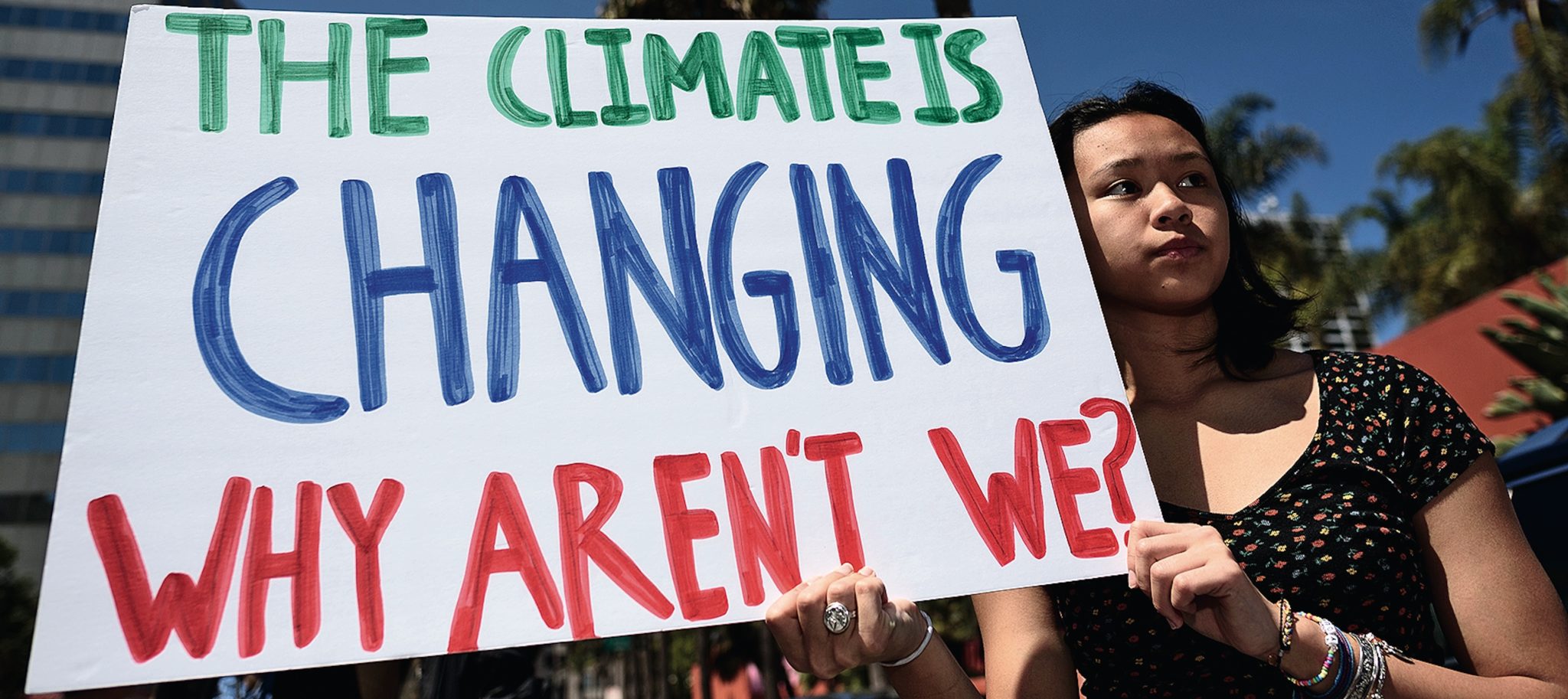 Girl holding a sign that says 'the climate is changing why aren't we?