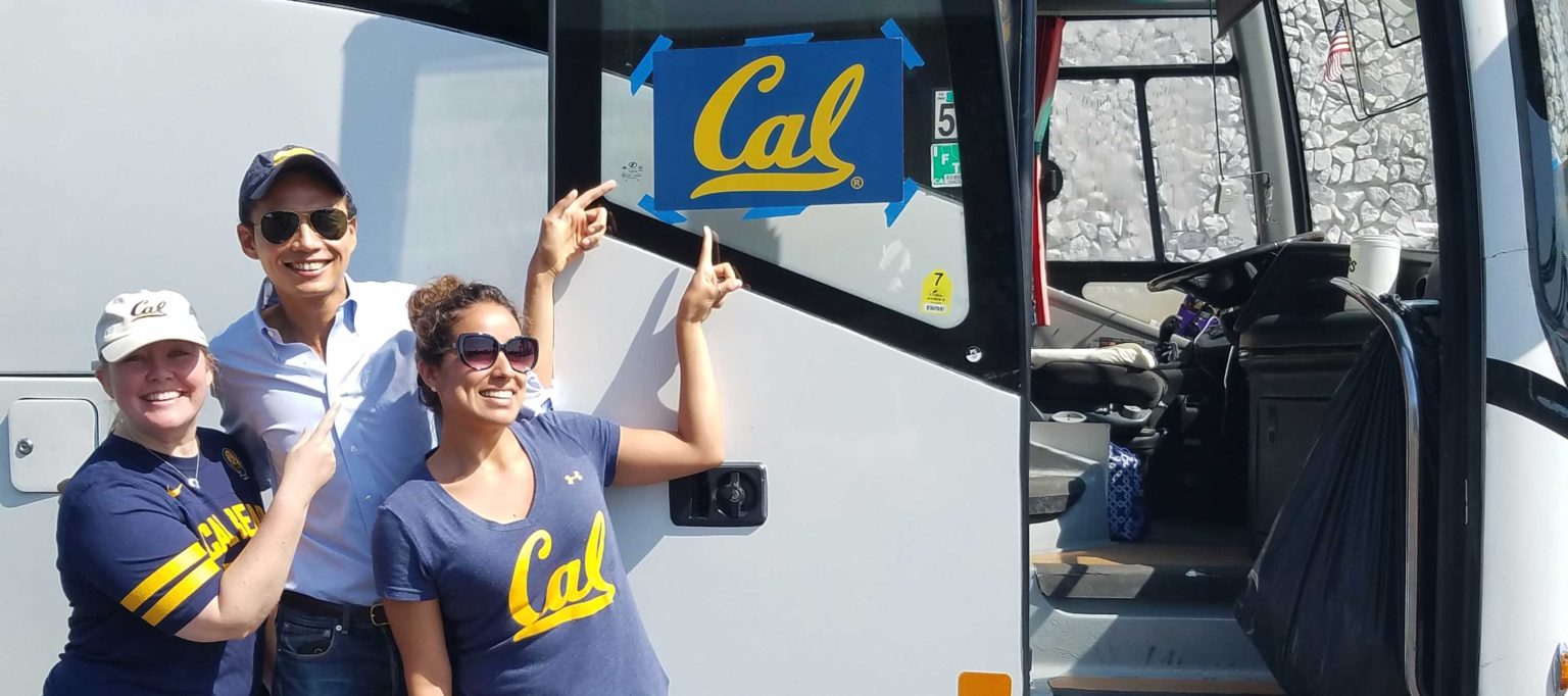 three people point to Cal sign on bus