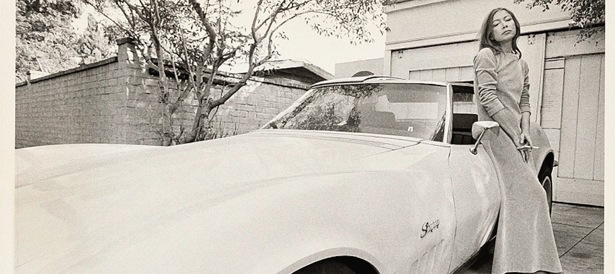 Joan Didion leaning against a car