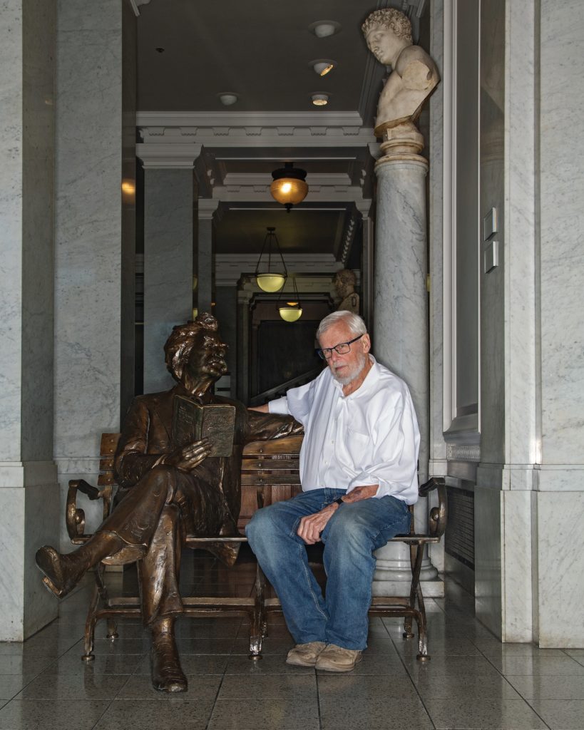 Hirst sitting next to a statue of Twain