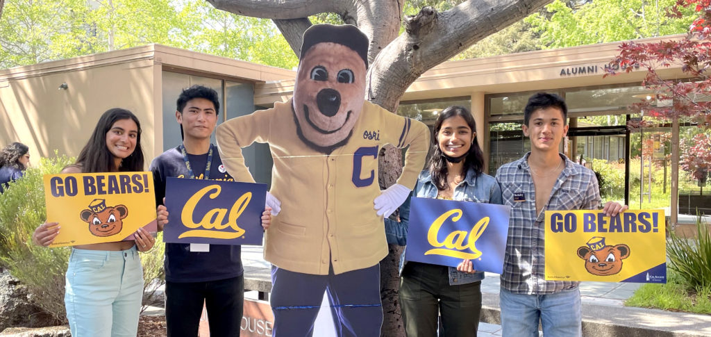 four students holding go bears signs stand with a cardboard Oski outside of Alumni House