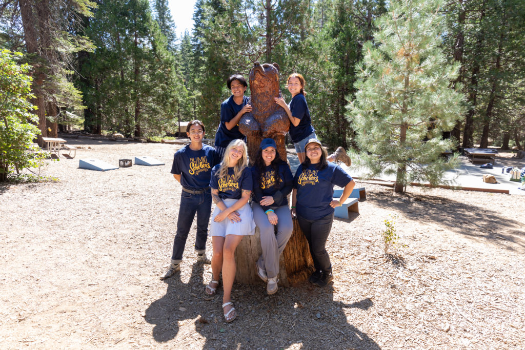A group of 6 students pose with a carved wooden bear statue.