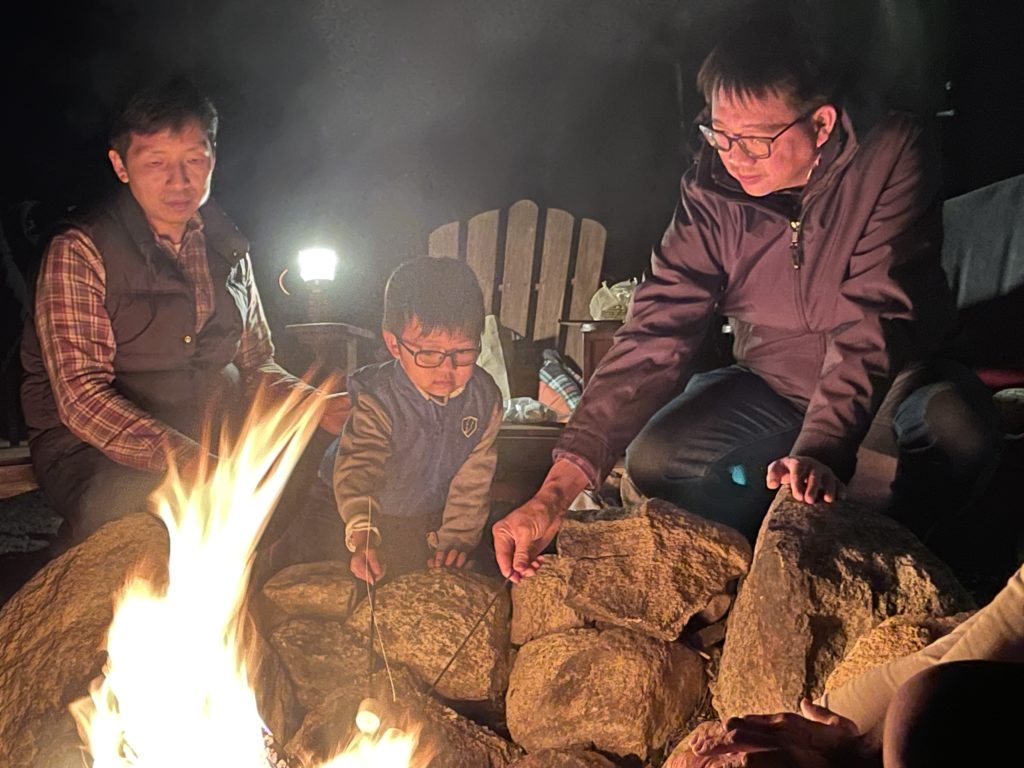 Two men and a boy making s'mores over a campfire