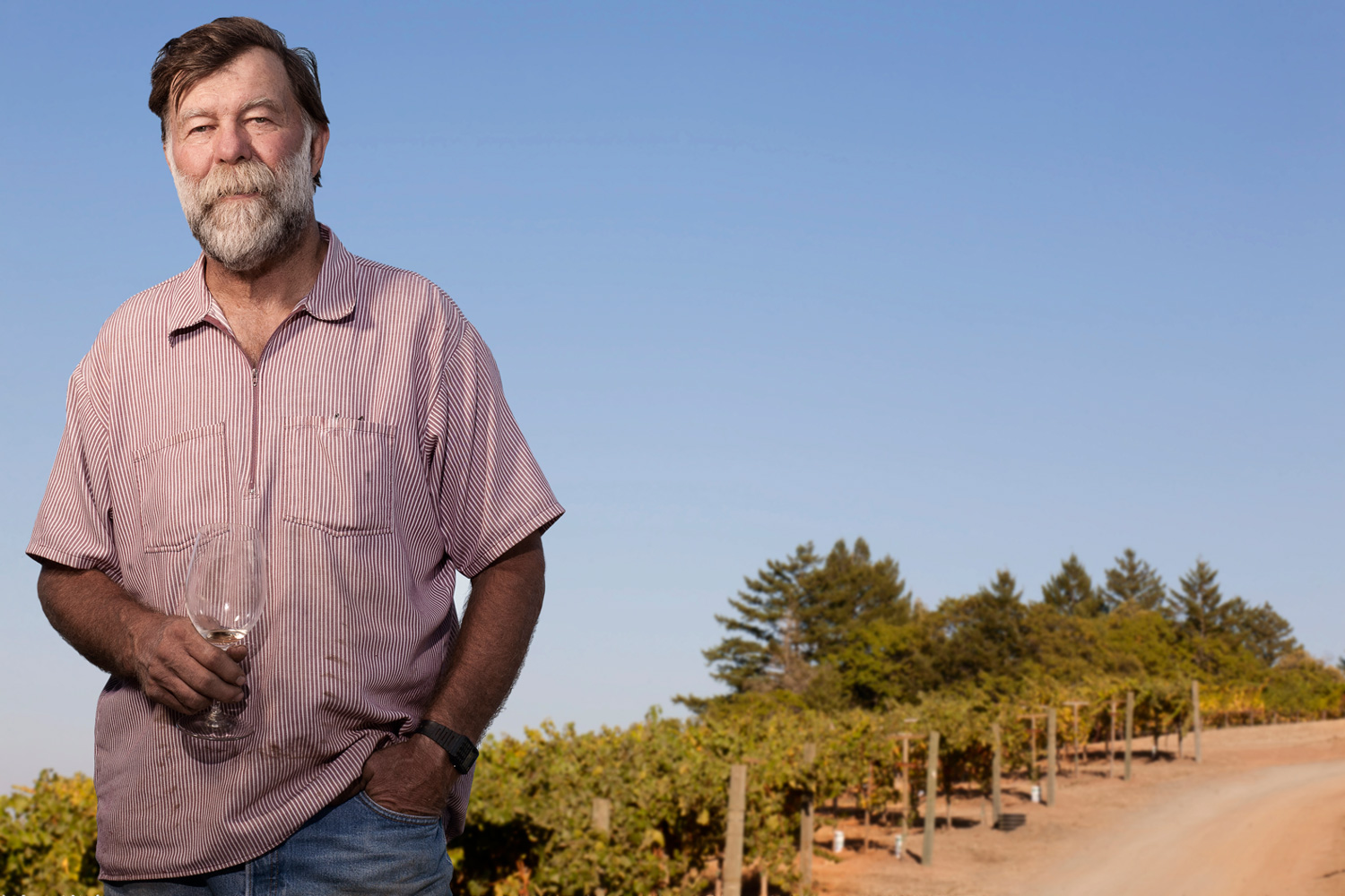 Business owner and winemaker Stuart Smith poses in front of a vineyard with a wine glass.