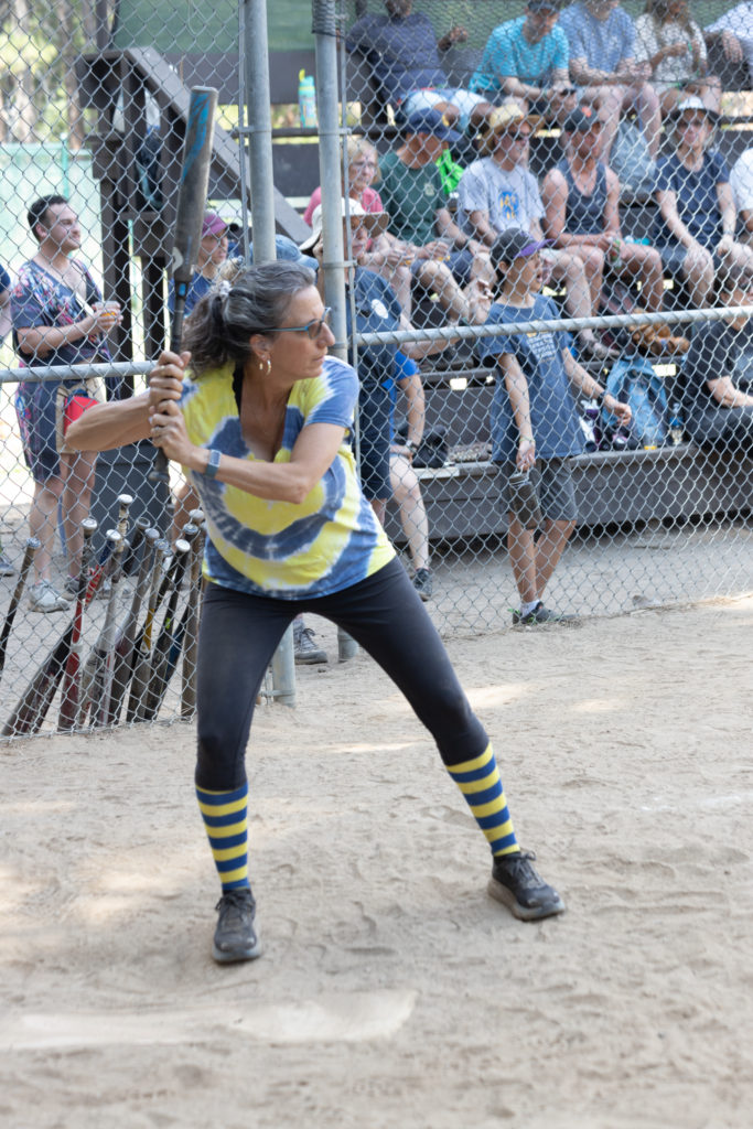 A woman in a tie-dye jersey getting ready to hit a softball.