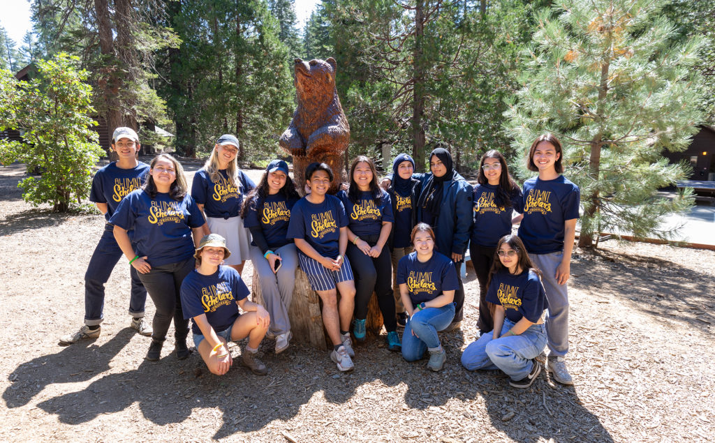A group of alumni scholars with a wooden bear statue at the Lair of the Golden Bear.