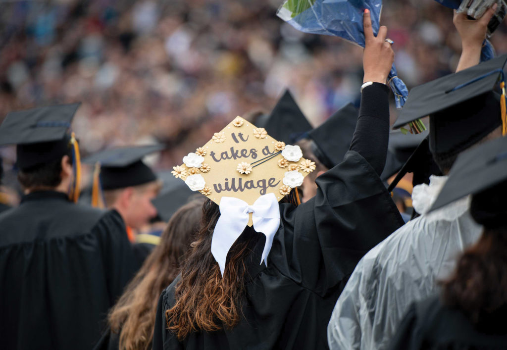 A graduate at commencement wearing a graduation cap decorated with the words 