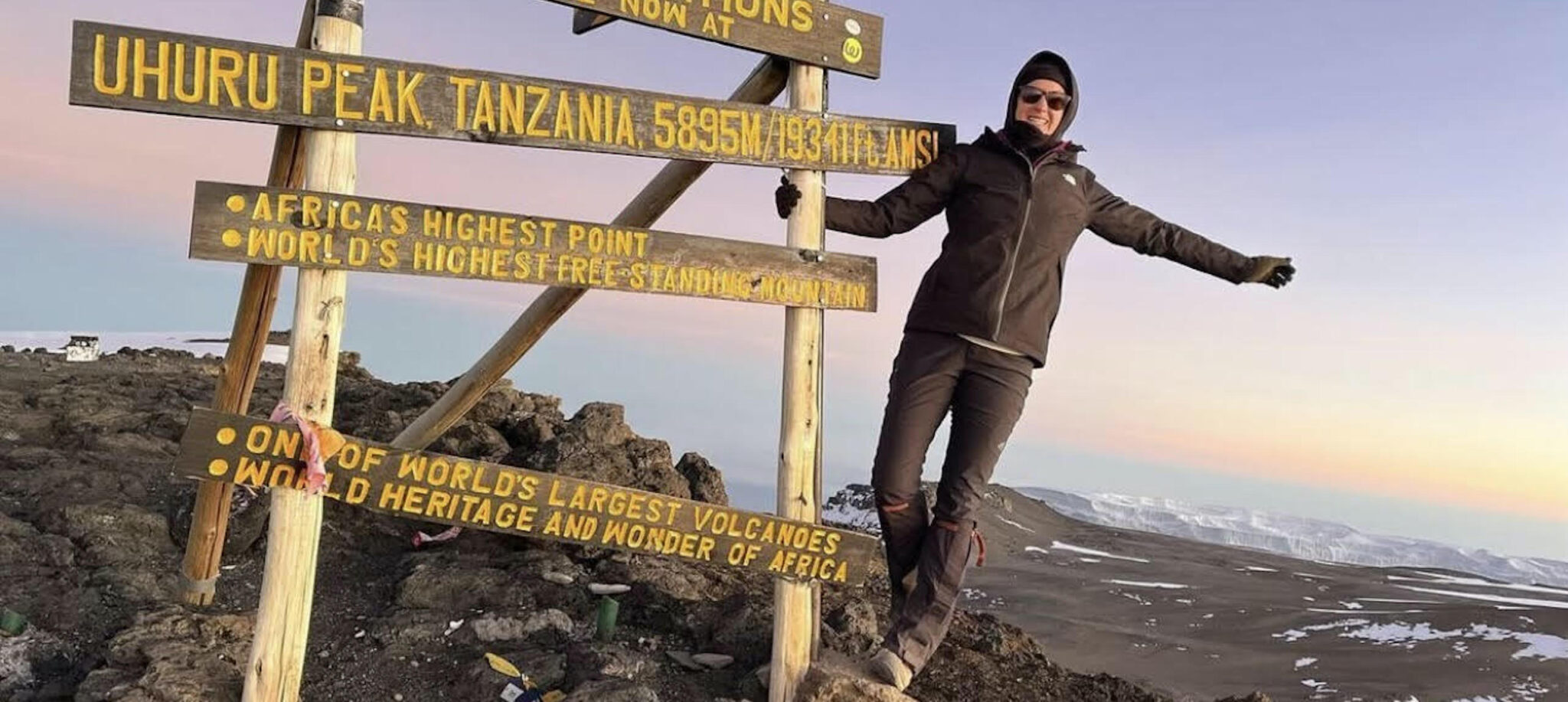 Shawn hanging off the sign at Mt Kilimanjaro