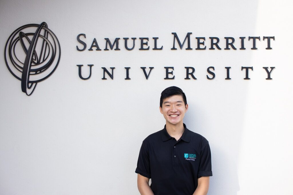 Robert Yu poses in front of the logo of Samuel Merritt University. 