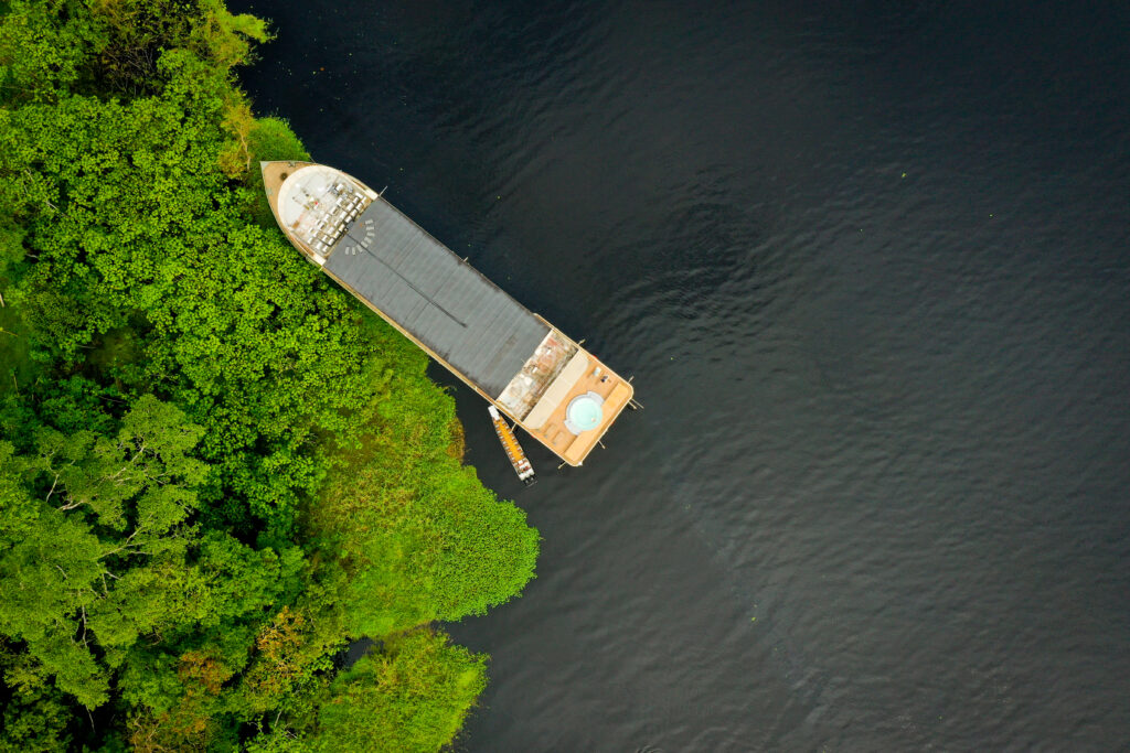 An aerial view of the Delfin III ship anchored along the lush, green shores of the Amazon River