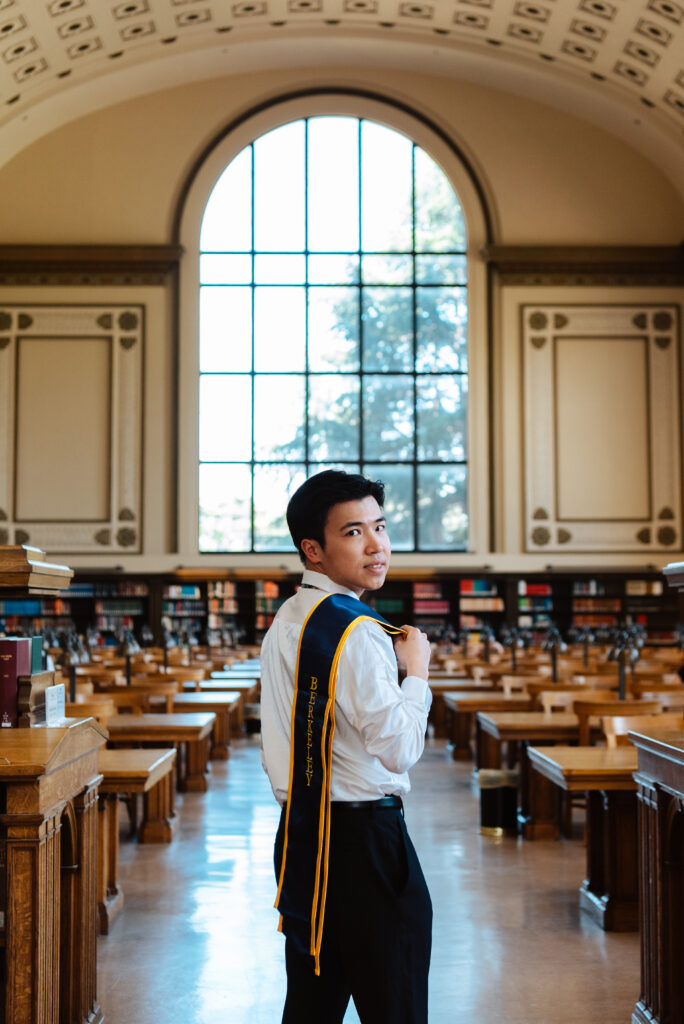 A Berkeley graduate poses inside a library with his stole over his shoulder.