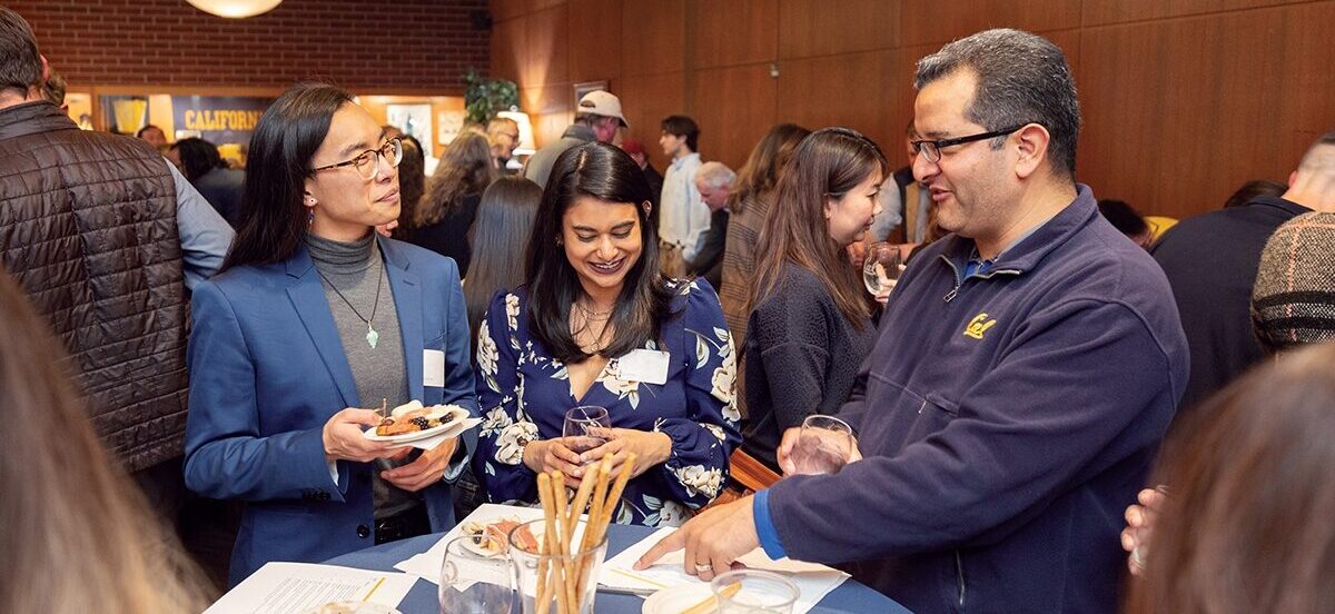a group of 3 people talk around a cocktail table at a wine tasting event at alumni house