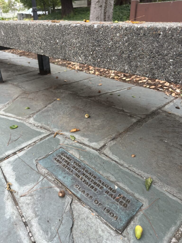 Th plaque on the bench at Alumni House that says: "Come you again along her paths: Her nurture raised and still sustains.”