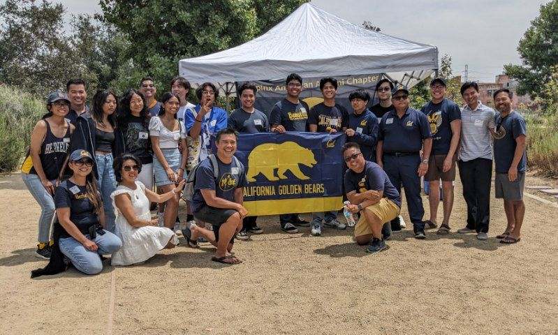 People at the Pilipinx American Alumni Chapter Summer Welcome Party pose with a Cal flag. 