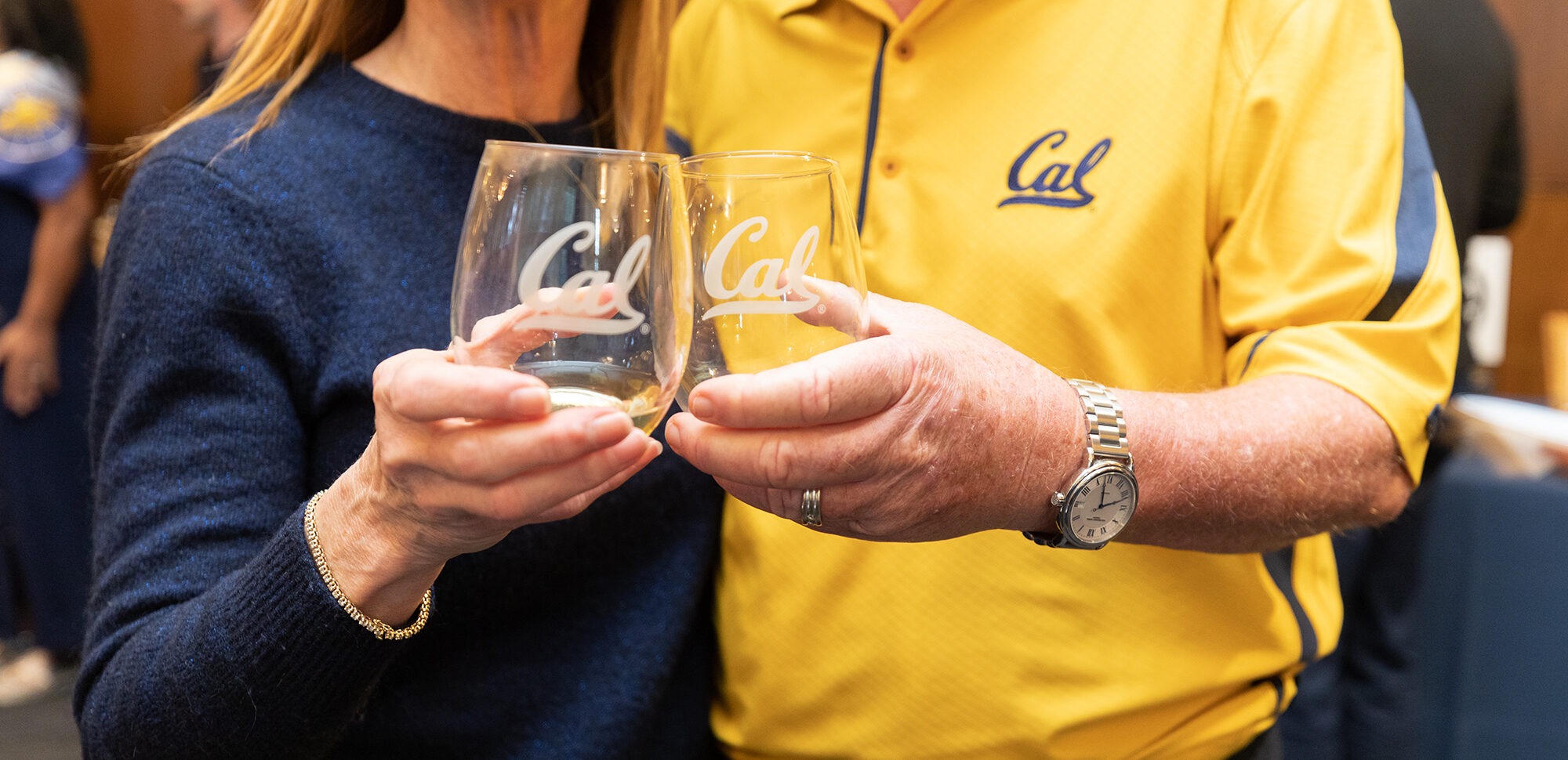 2 people toasting with Cal wine glasses and one is wearing Cal logo shirt
