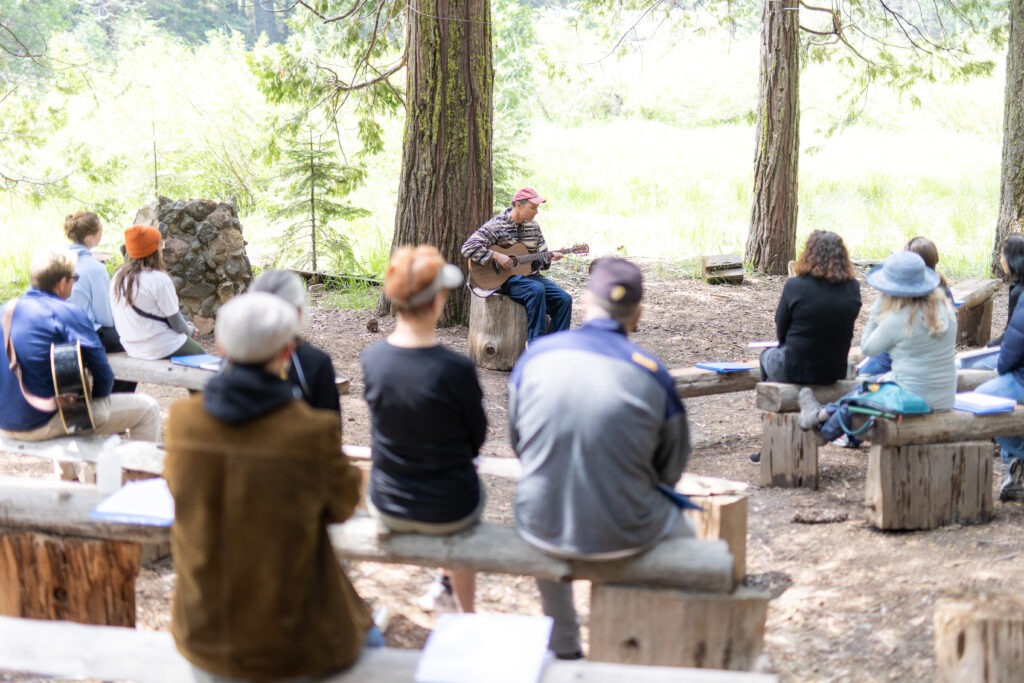 a man playing guitar amongst pine trees to an audience