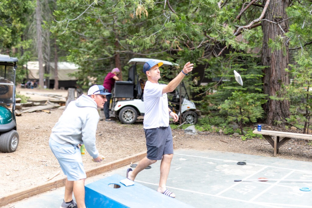 two adults playing cornhole, one mid throw