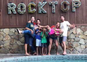 A family making funny faces and poses in front of a sign that says "Rocktop"