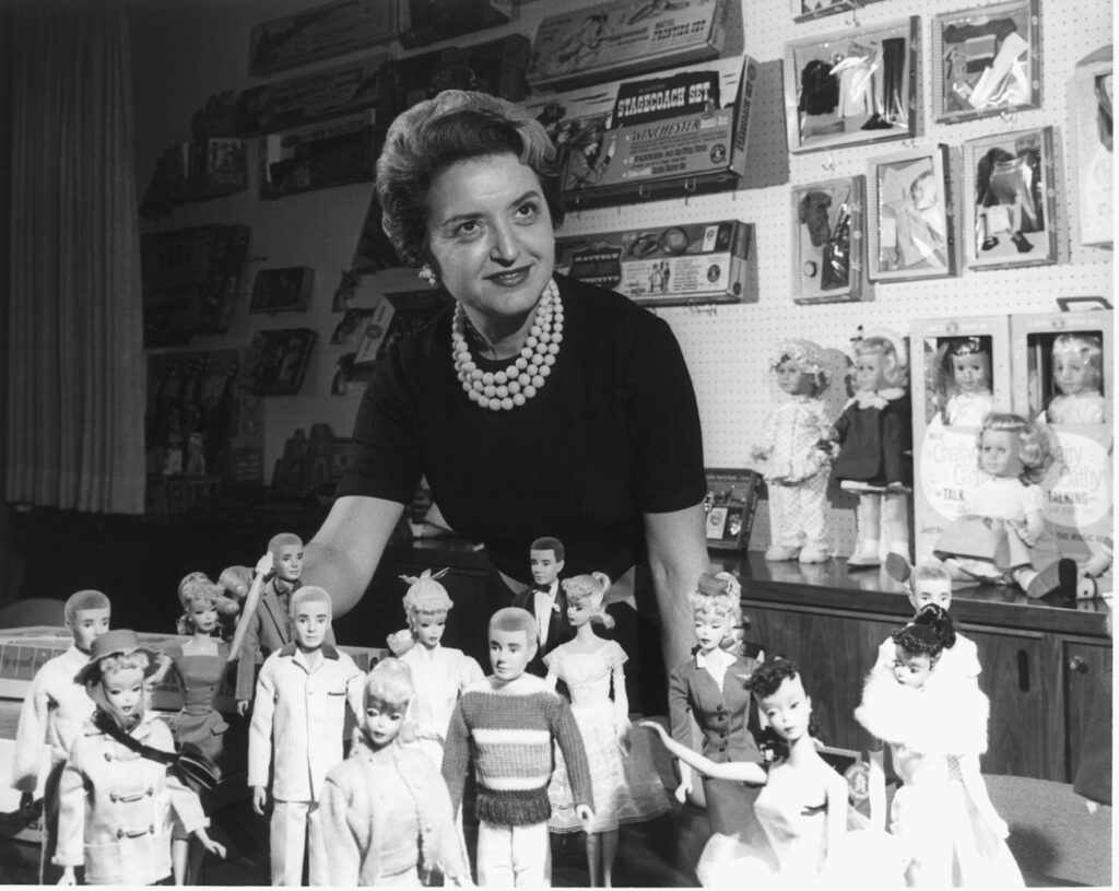 Ruth Handler posing behind Barbies