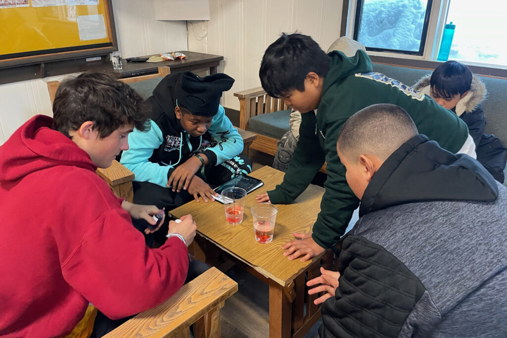 4 boys sitting around a table engaged by a science experiment