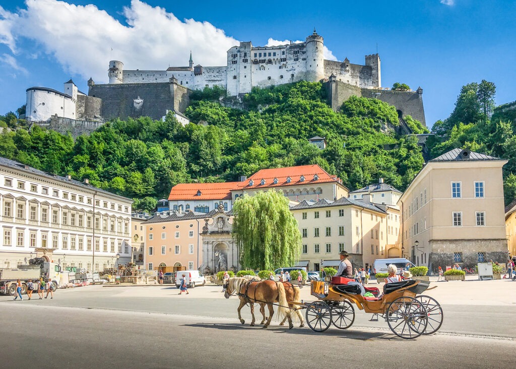 panoramic view of the historic city of Salzburg with traditonal horse-drawn Fiaker carriage and famous Hohensalzburg Fortress on a hill on a sunny day with blue sky and clouds in summer