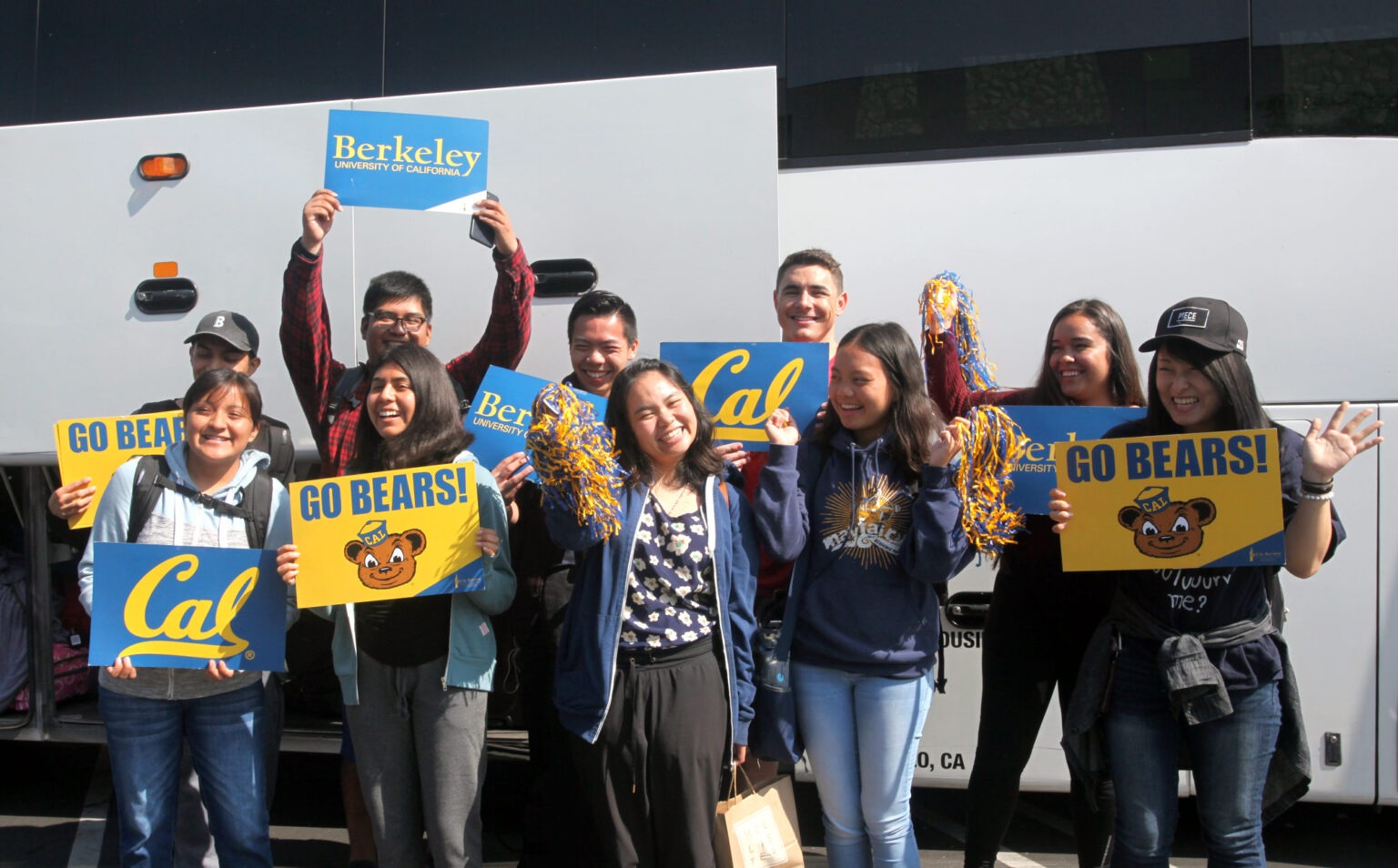 students hold cheer cards in front of a bus