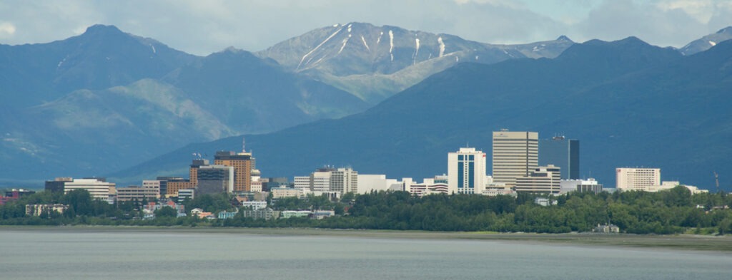 panoramic city view with water in foreground and mountains in background