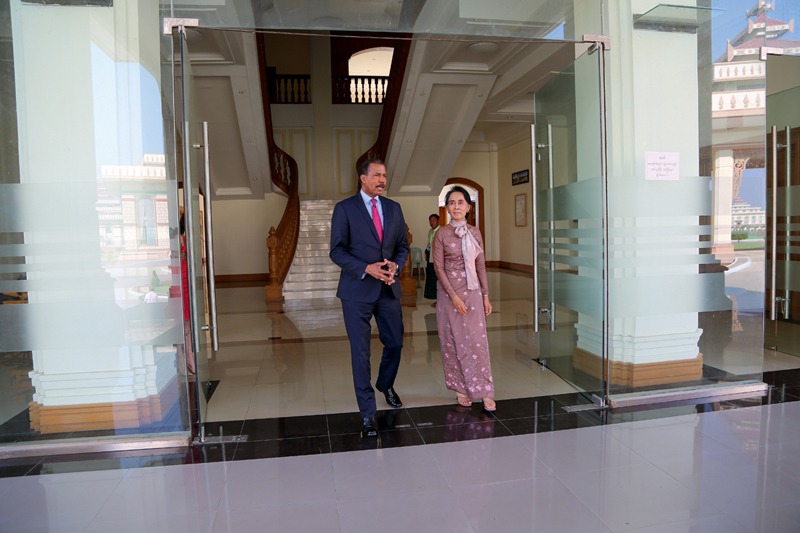 Burmese leader Aung San Suu Kyi and Bill Whitaker walk together through the entrance of an elegant building.