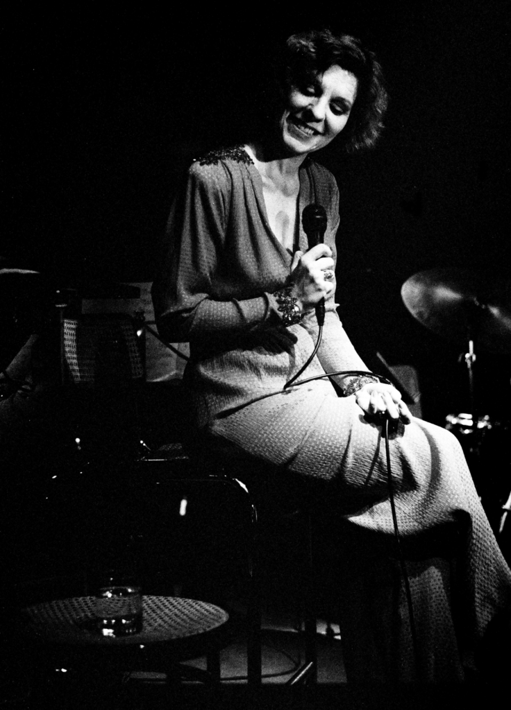Black and white photo of Susannah McCorkle on stage smiling and holding a microphone.