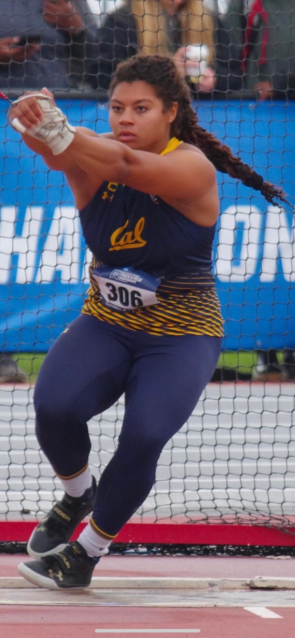 Track and field athlete Camryn Rogers, wearing a blue and yellow Cal uniform, is captured in action during a hammer throw event.