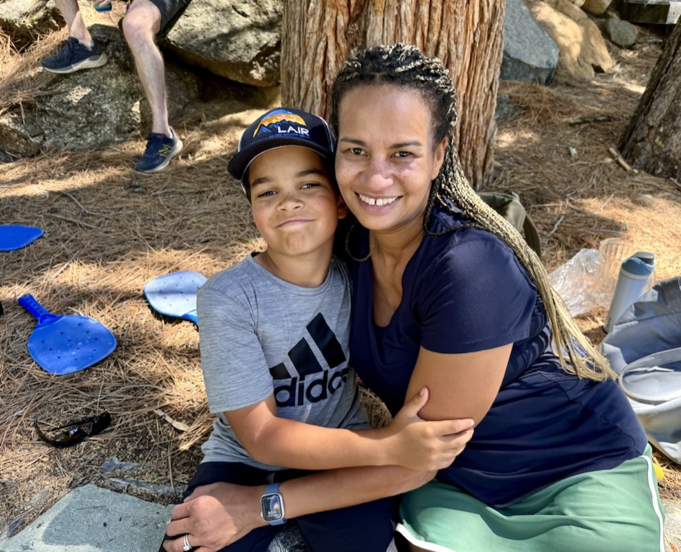 Adult and child wearing a Lair cap sitting side-by-side, smiling, and hugging.