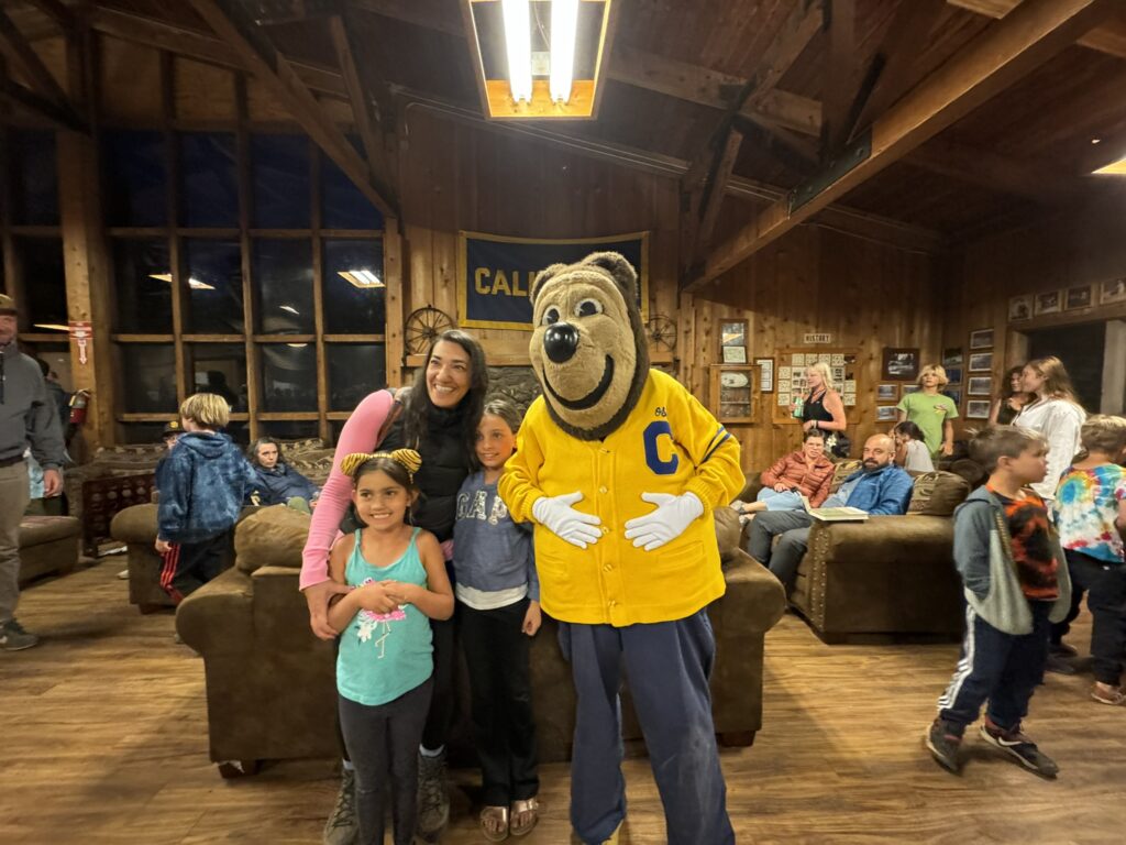 Oski standing with a smiling woman and two children inside the lodge.