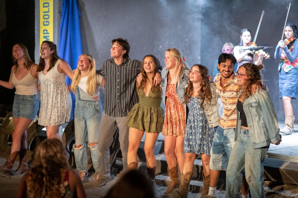 A group of staffers arm in arm singing in front of the stage during the Camp Gold Hootenany.