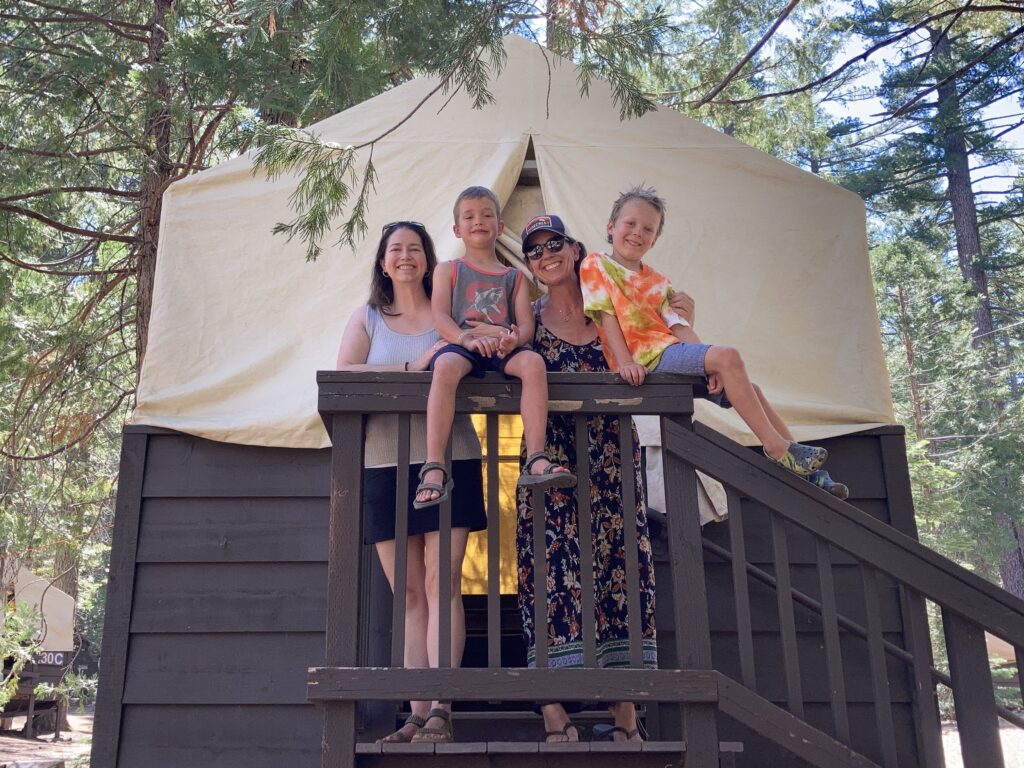 two adults and two children standing, smiling outside their tent