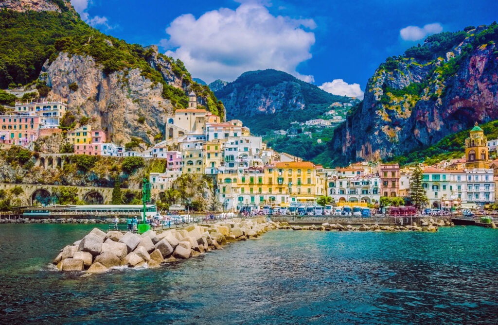 Colorful coastal village nestled between mountains, featuring vibrant buildings along the shore and rocky jetty extending into the water