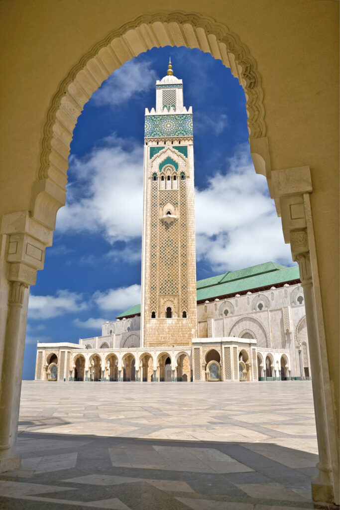 A majestic view of Hassan II Mosque's minaret framed by an ornate arch, under a clear blue sky.