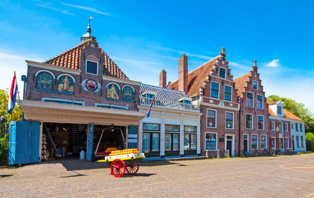 Historic Dutch architecture with colorful facades and a yellow cart filled with oranges, under a bright blue sky